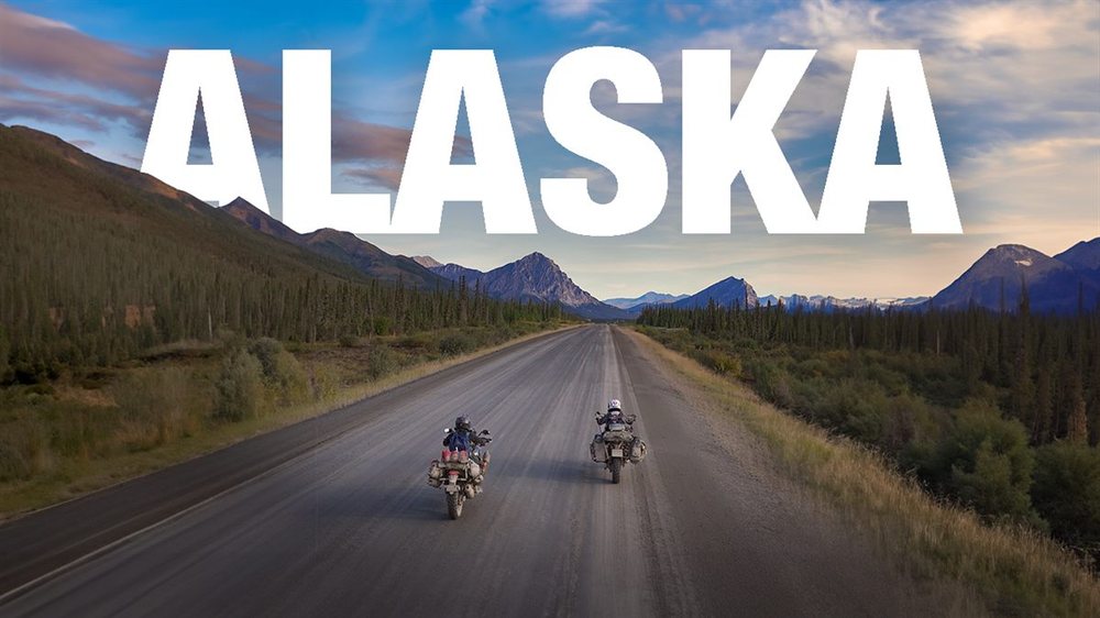 Carretera atravesando montañas y bosques boreales en Alaska, dos motos rodando al atardecer